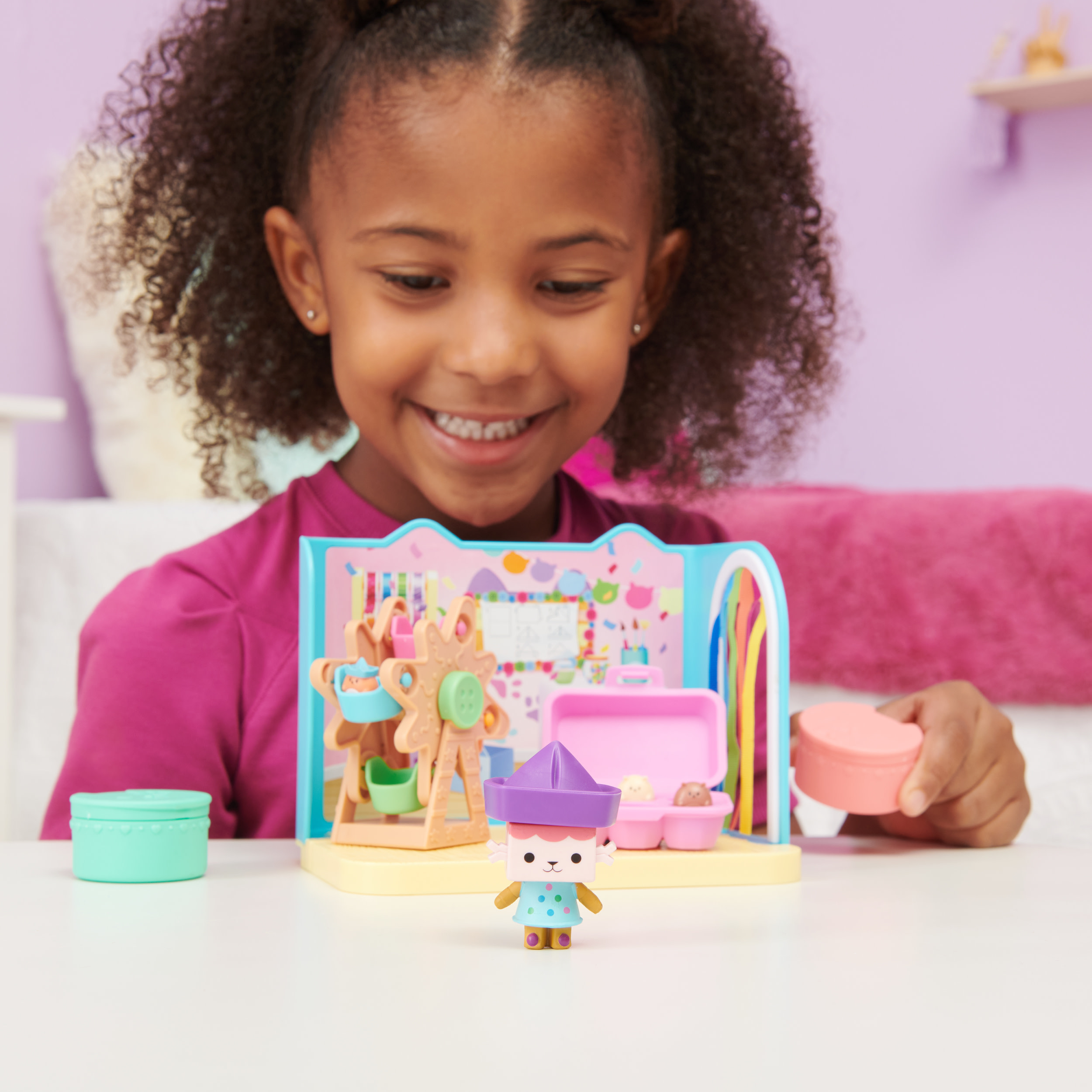 Ein junges Mädchen lächelt über ein Spielzeug-Spielset. Das Set beinhaltet ein Riesenrad und Spielfiguren.