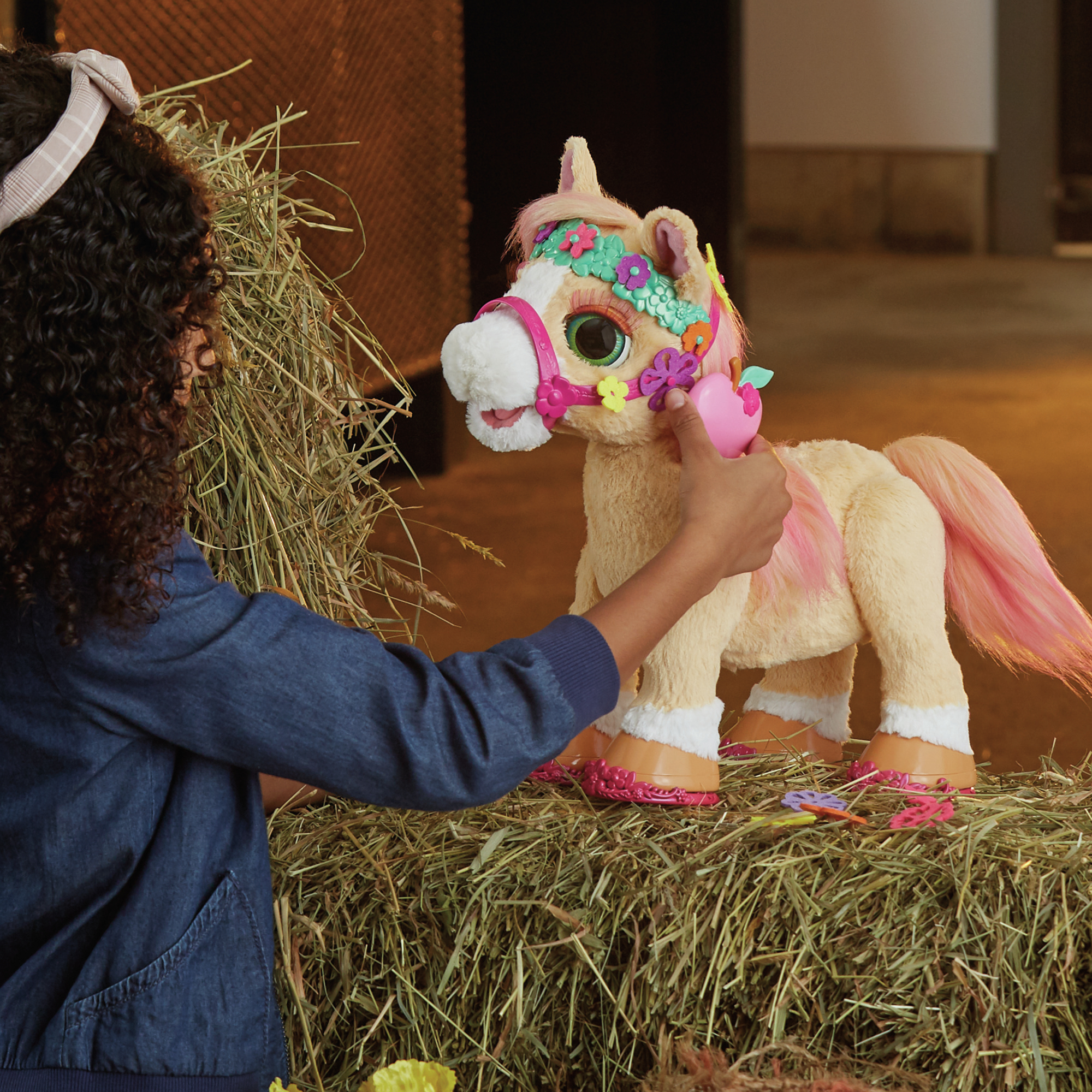 Ein Kind interagiert mit einem Spielzeugpferd auf Heu. Das Pony ist rosa, hellbraun und hat Blumenschmuck.