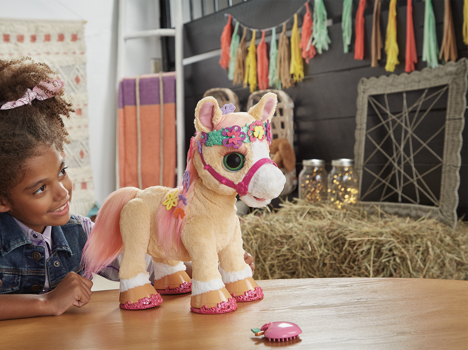 Una niña con un caballo de juguete, en una mesa. Un fardo de heno y decoración detrás.