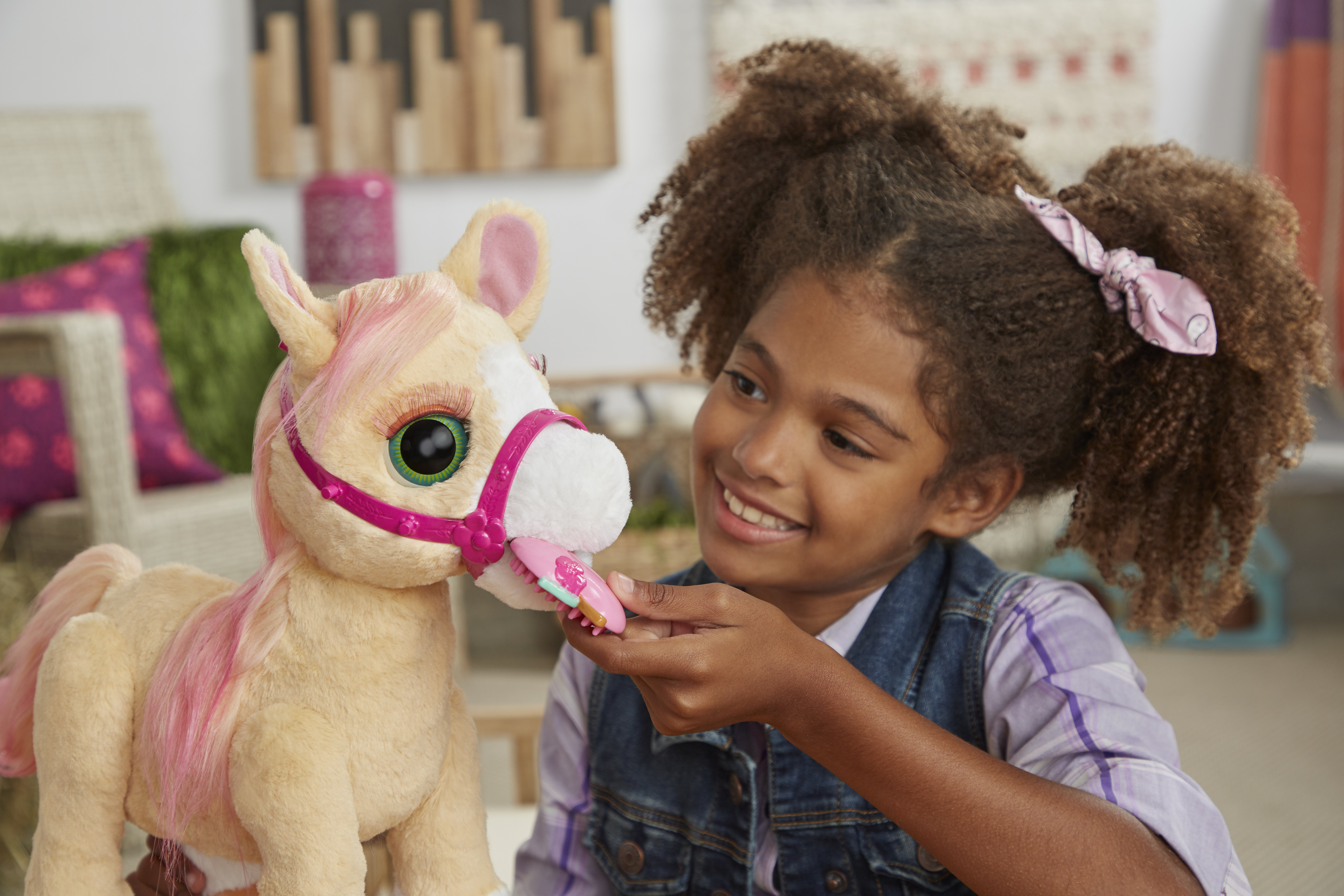 Una niña sonríe mientras acaricia un caballo de peluche. Un cepillo está en la boca del caballo.