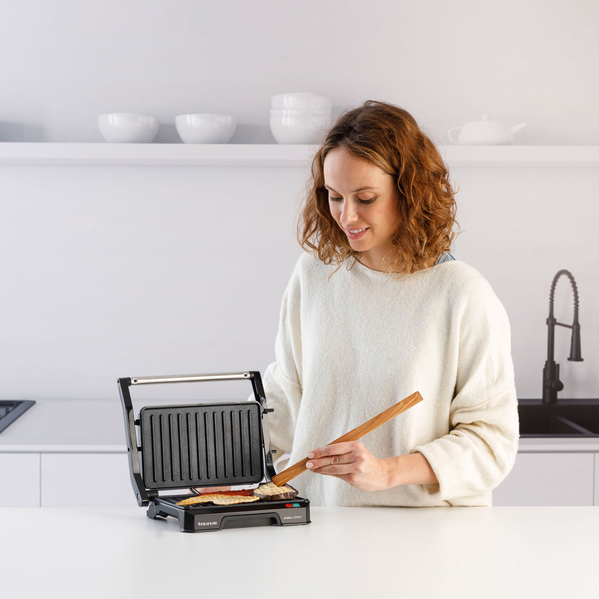 Kobieta gotuje na prasie do panini, używając drewnianej szpatułki do przewracania jedzenia.