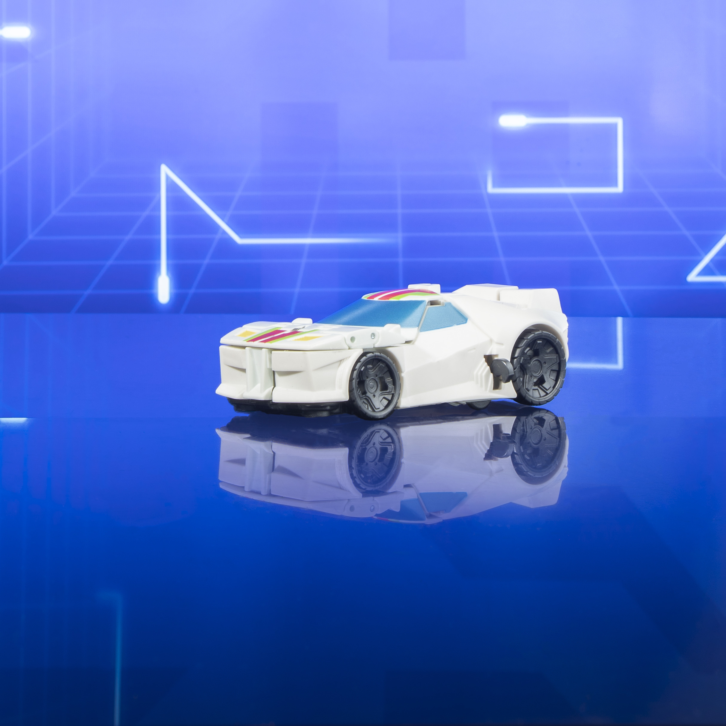 Biały samochodzik zabawka umieszczony na odblaskowej niebieskiej powierzchni, z niebieskim wzorem linii w tle.