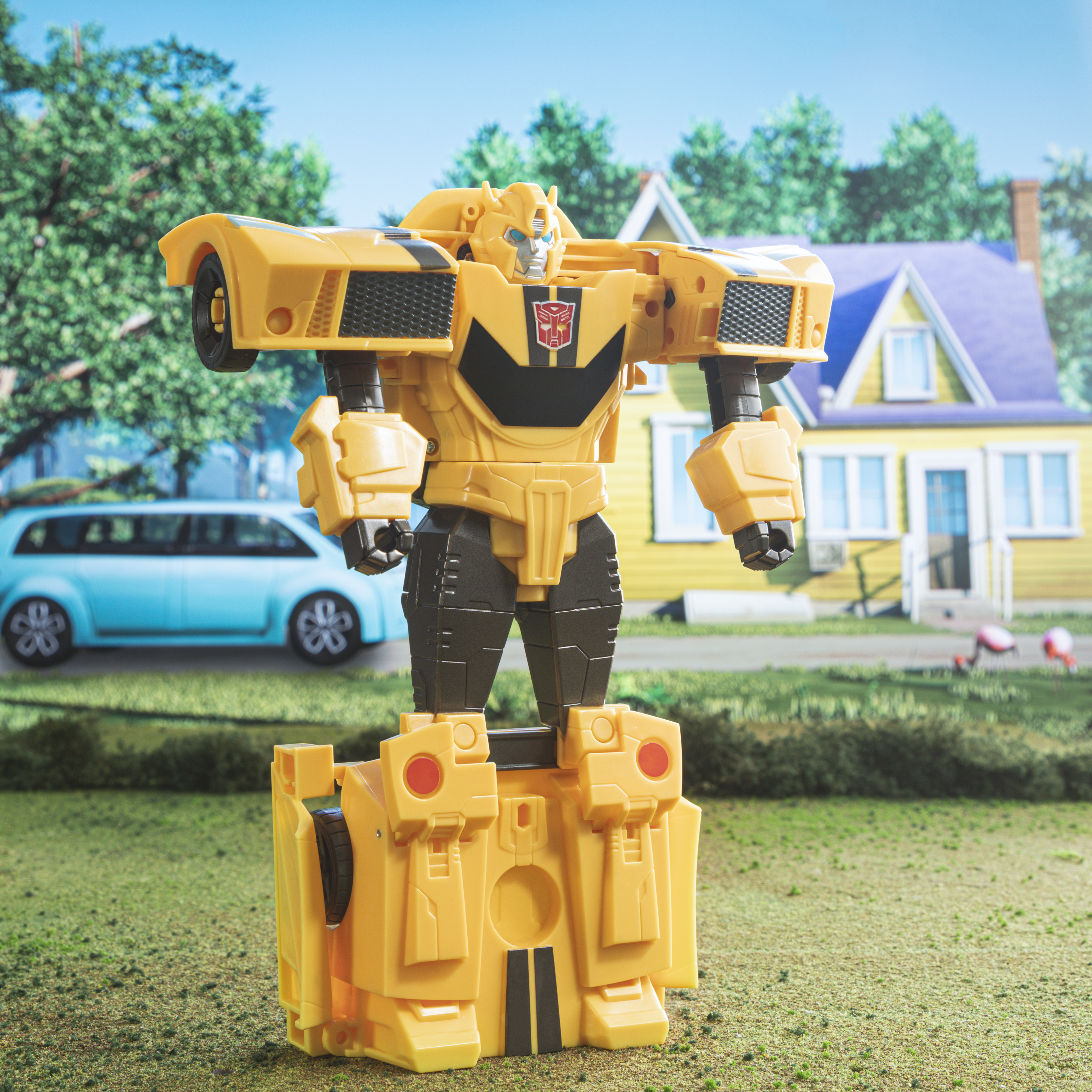 Robot Transformer amarillo en forma de coche, de pie sobre una base, con telón de fondo suburbano.