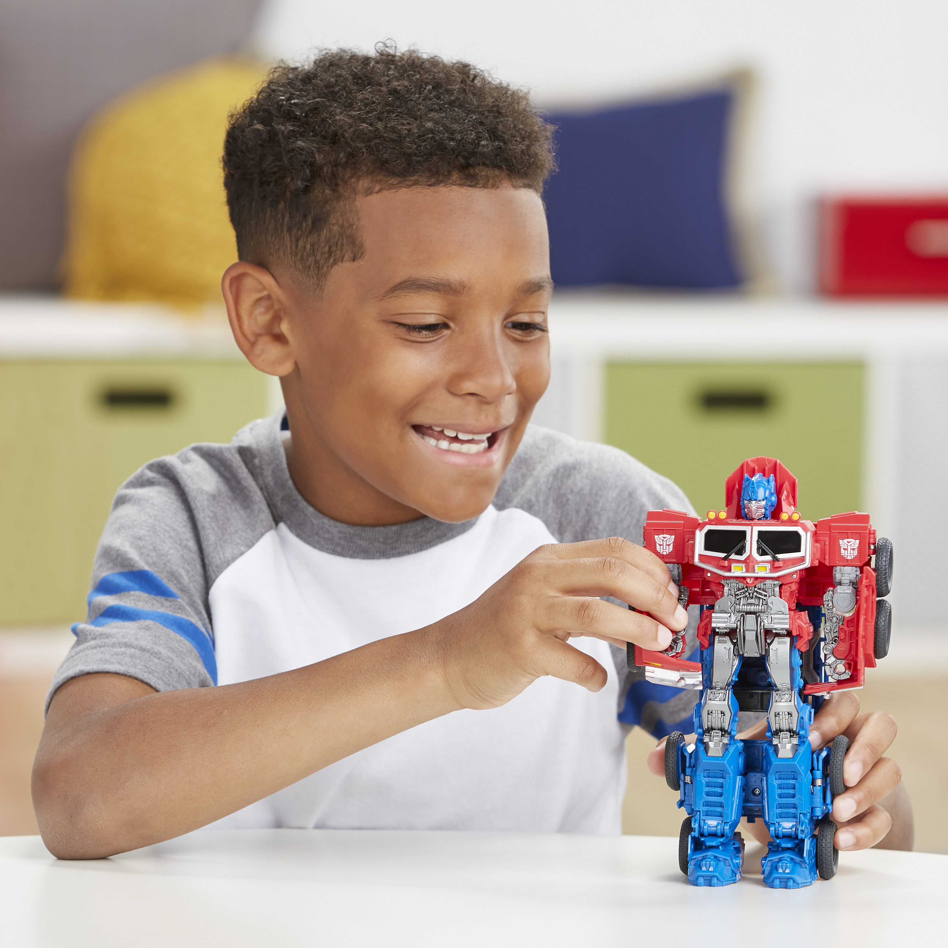 Uśmiechnięty chłopiec trzymający czerwoną i niebieską zabawkę Transformers, gotowy do akcji.