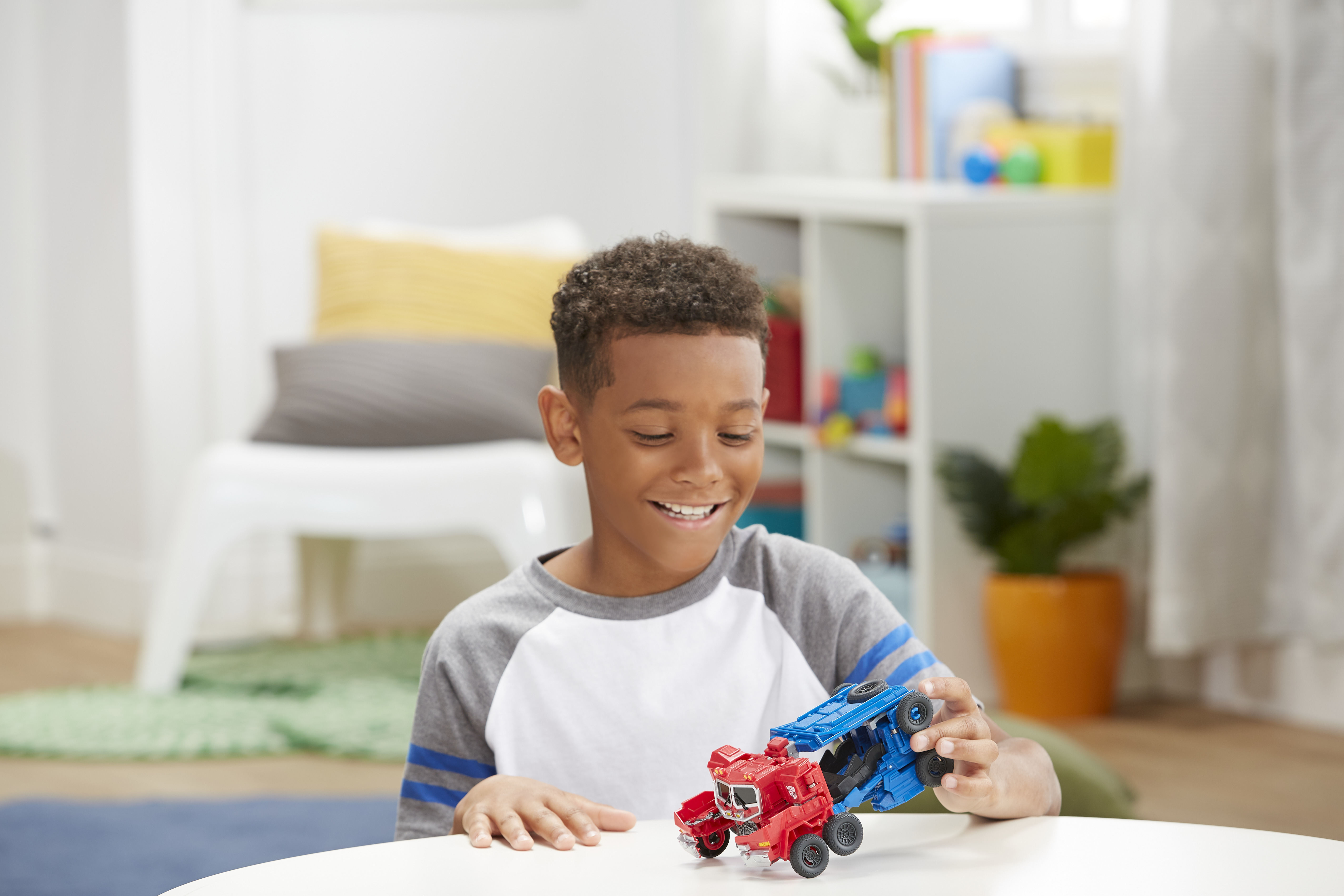 Mały chłopiec uśmiecha się, trzymając czerwoną i niebieską ciężarówkę na białym stole.