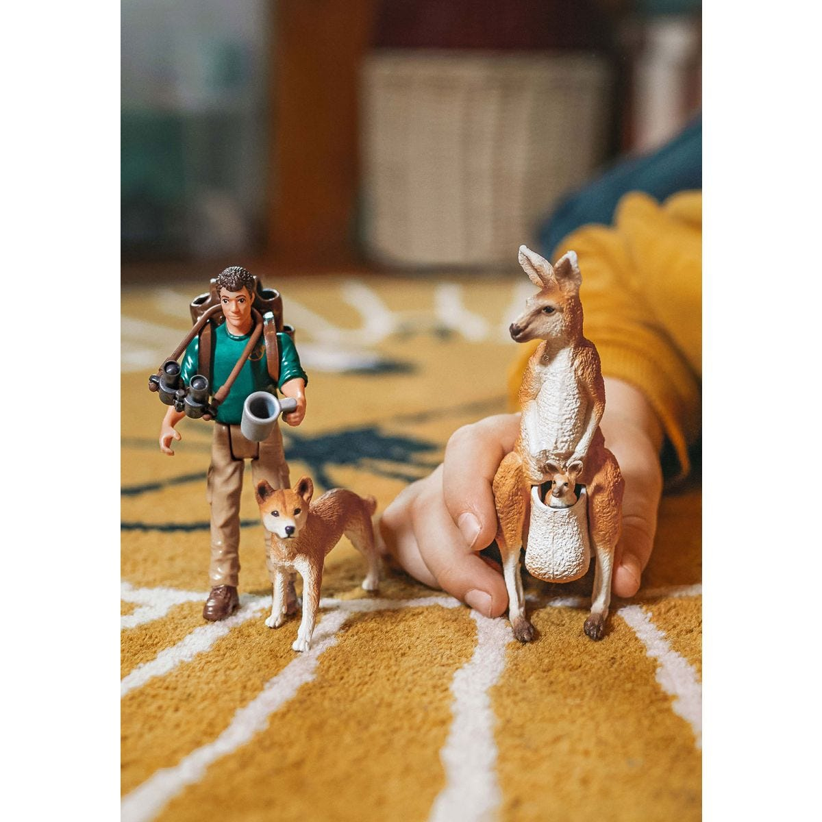 Spielfiguren: Mann, Hund und Känguru mit Jungtier. Szene auf gelbem, gemusterten Teppich.