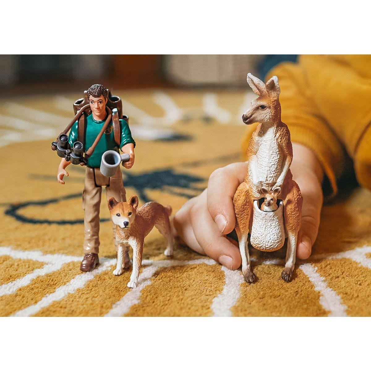 Ein Mann mit einem Hund und ein Känguru mit einem Babykänguru im Beutel. Die Umgebung ist im Freien.