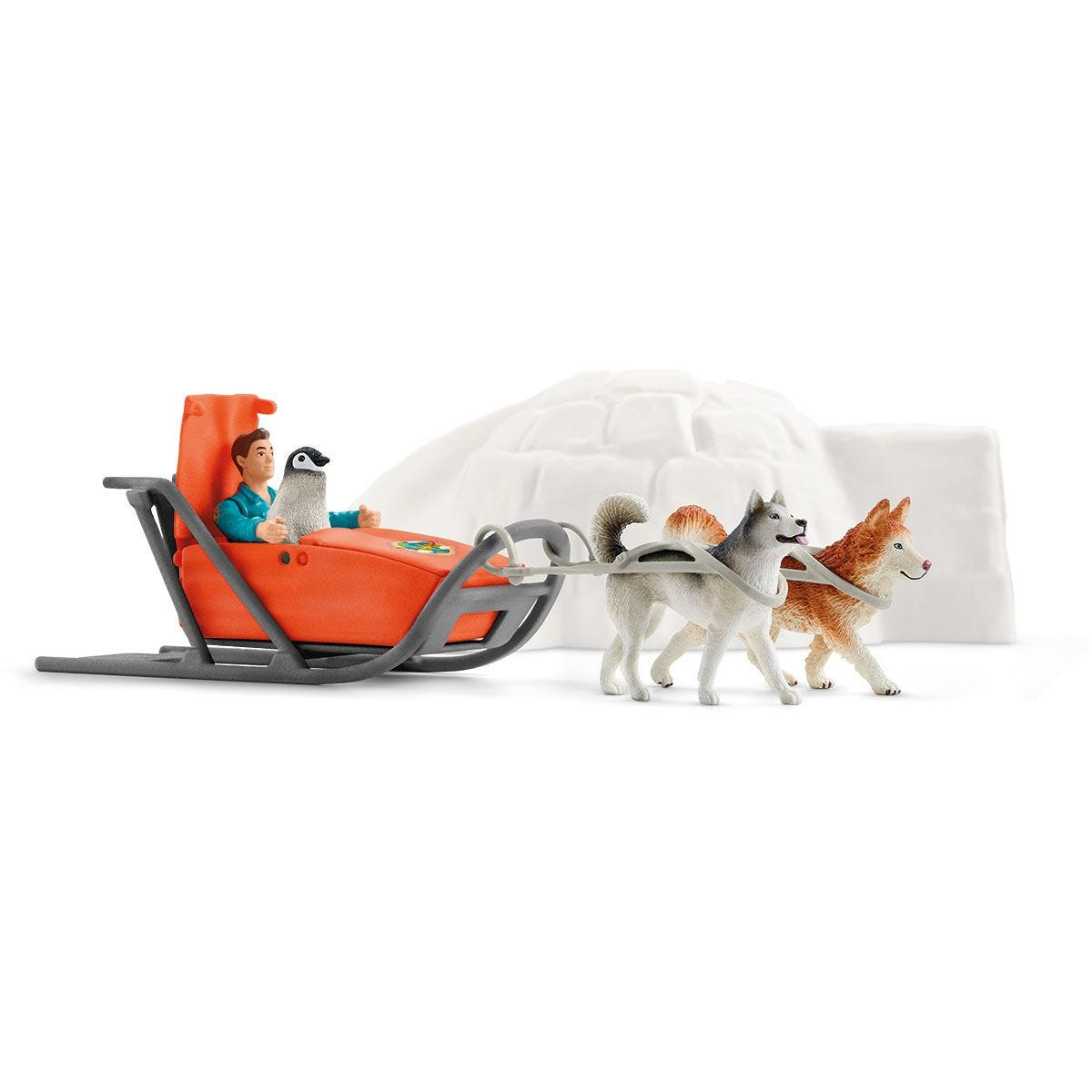 Des chiens husky jouets tirent un traîneau orange avec une personne et un pingouin. Un igloo est en arrière-plan.