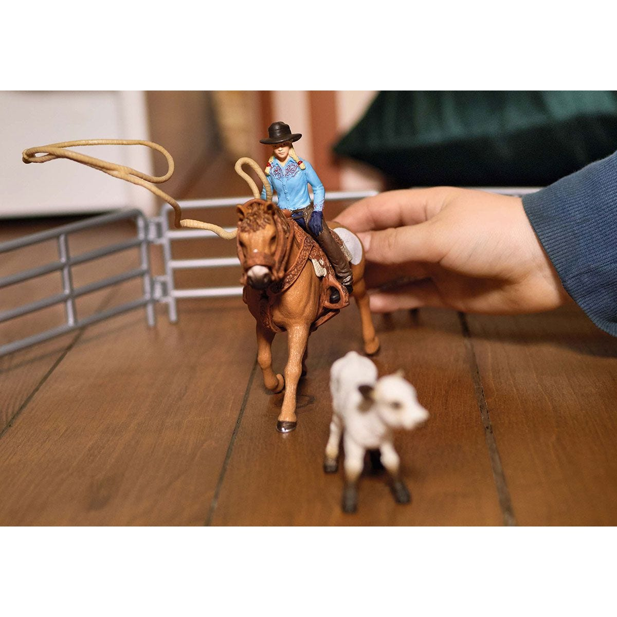 A toy scene of a cowboy riding a horse, roping a steer in a pen.