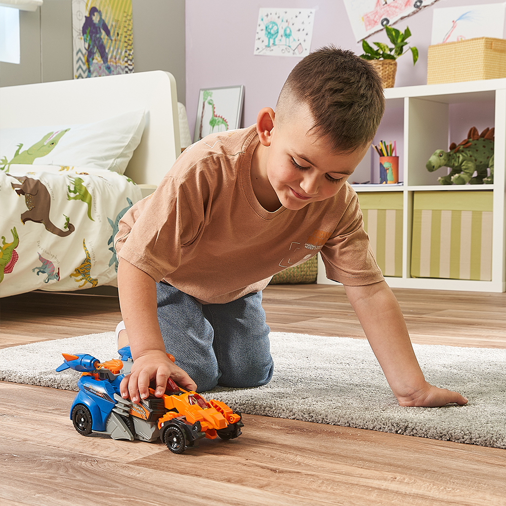 Ein kleiner Junge spielt mit einem Spielzeugauto in einem Zimmer mit Dinosaurier-Bettwäsche.