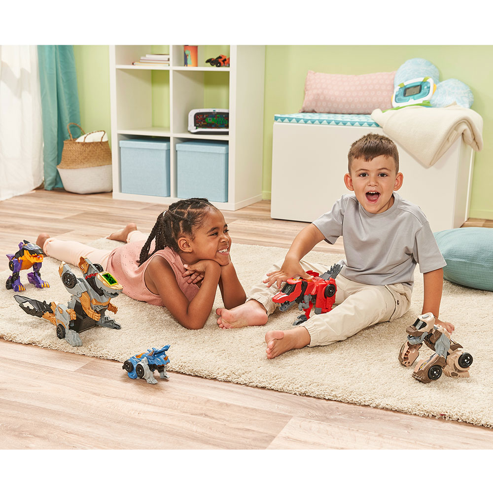 Zwei Kinder spielen mit Spielzeugdinosauriern auf einem beigen Teppich in einem Zimmer mit Spielzeug und einem Fenster.