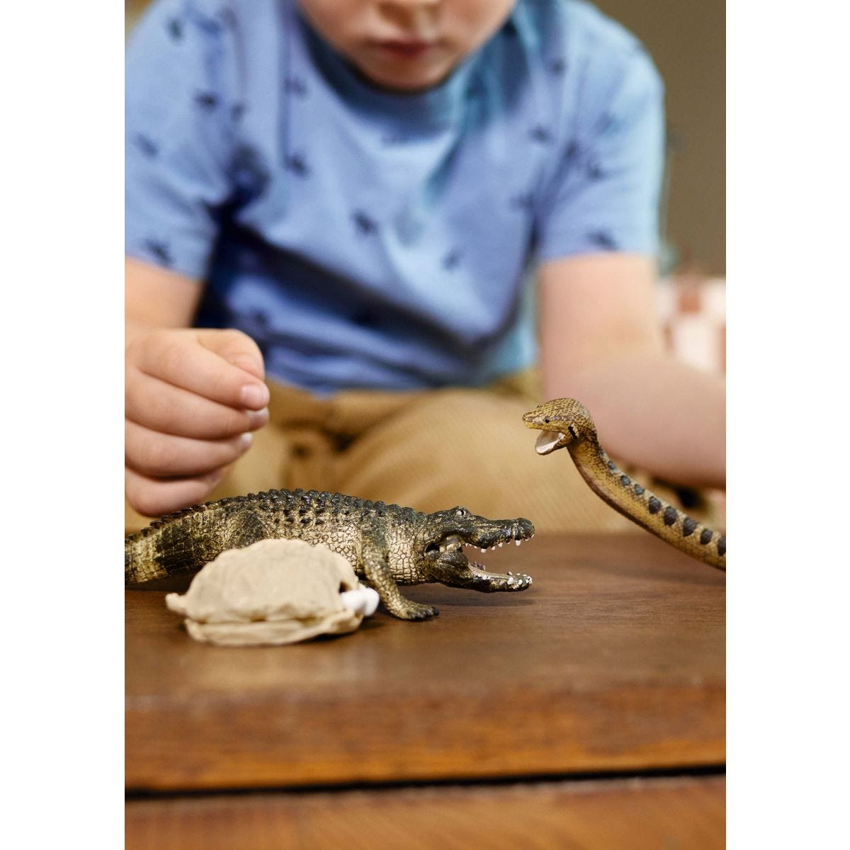 Ein Kind betrachtet Spielzeugkrokodil und Schlange. Das Krokodil ist grün und die Schlange braun.