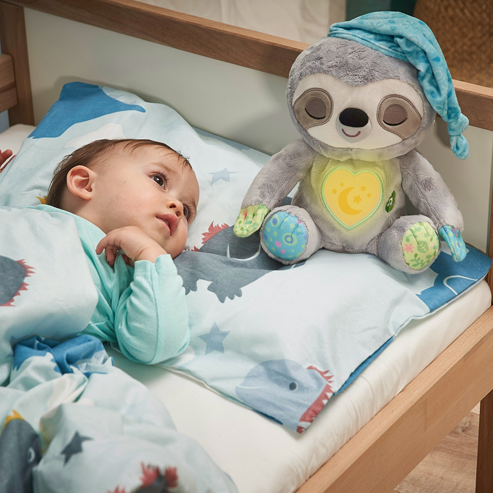 Ein Baby liegt im Bett neben einem Stofftier-Faultier. Das Baby schaut nach oben.