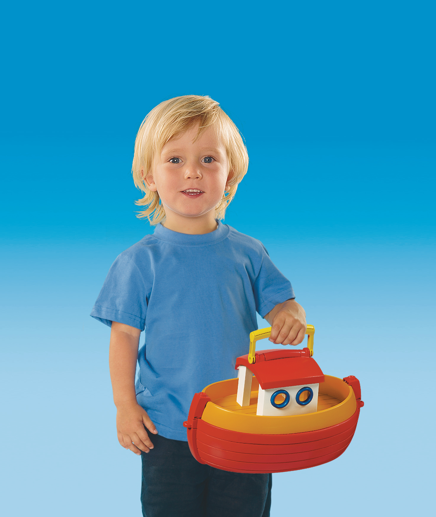 Ein lächelndes Kind hält ein Spielzeugboot mit rotem und gelbem Rumpf.