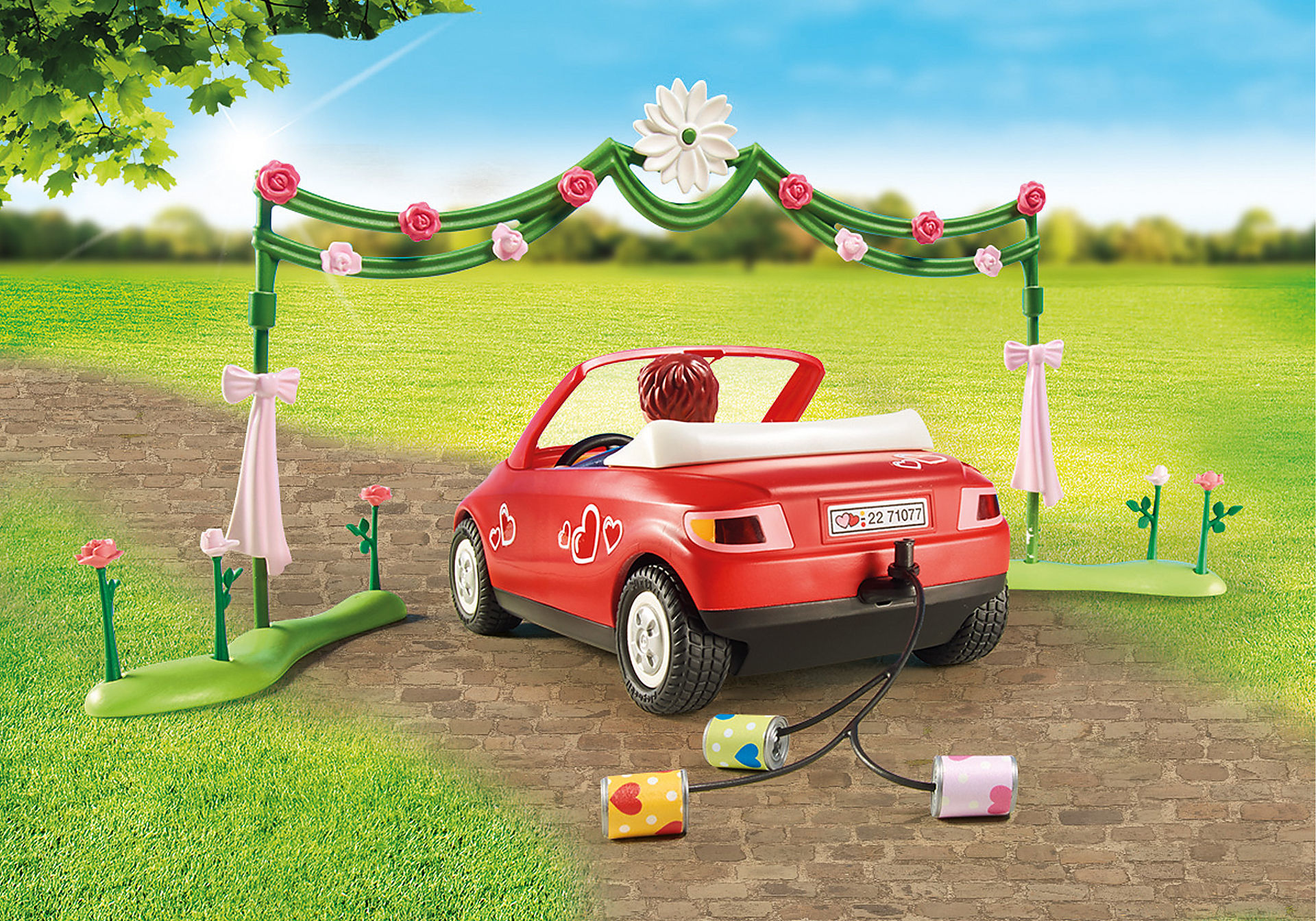 Eine Spielzeug-Hochzeitsszene mit einem roten Auto, einem dekorierten Torbogen und Blumendekorationen.