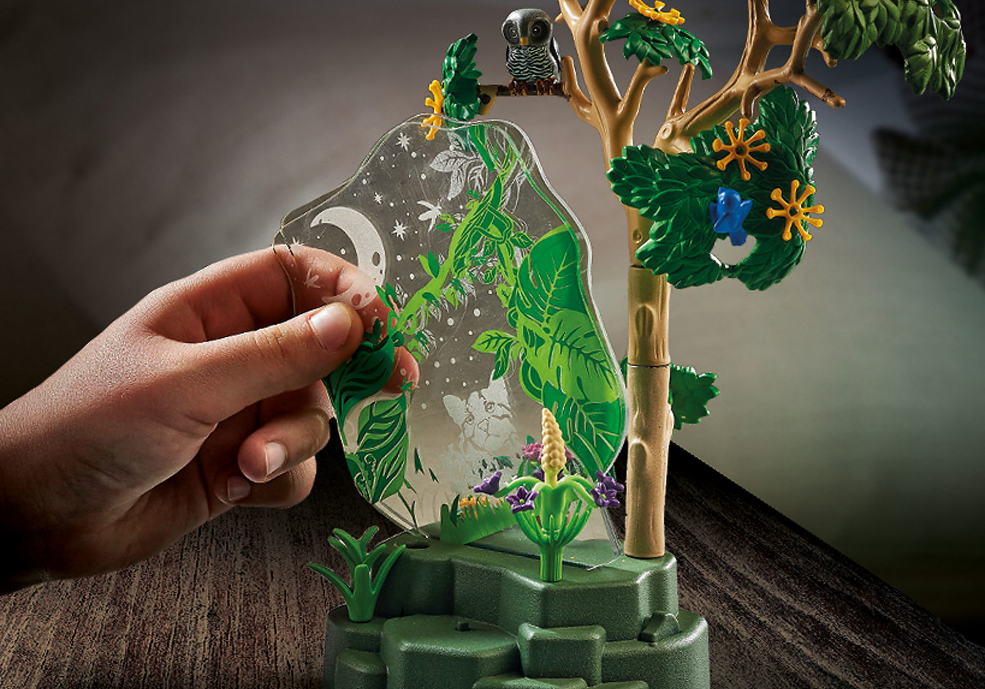 Ręka wchodzi w interakcję z przezroczystym wyświetlaczem ze sceną leśną, sową i innymi elementami.