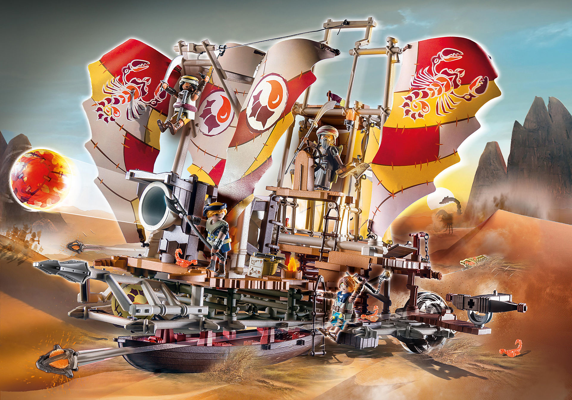 Spielzeugschiff mit Figuren in Wüstenszene. Große Segel, Figuren an Deck, Sanddünen im Hintergrund.