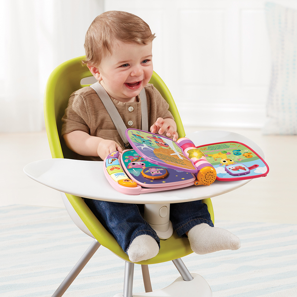 Baby in einem Hochstuhl, lacht, während es ein buntes Buch betrachtet.