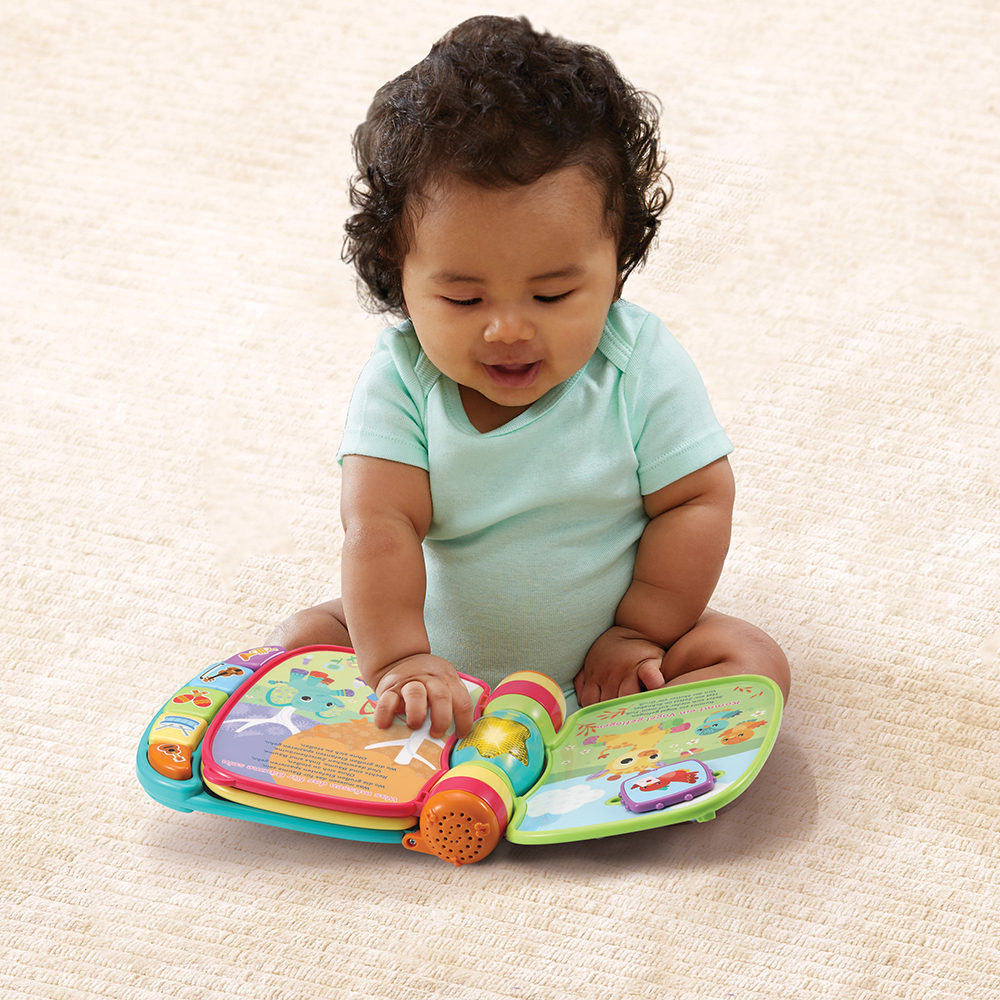 Ein Baby sitzt mit einem Buch. Das Buch ist offen und farbenfroh, mit einem Spielzeuglautsprecher in der Mitte.