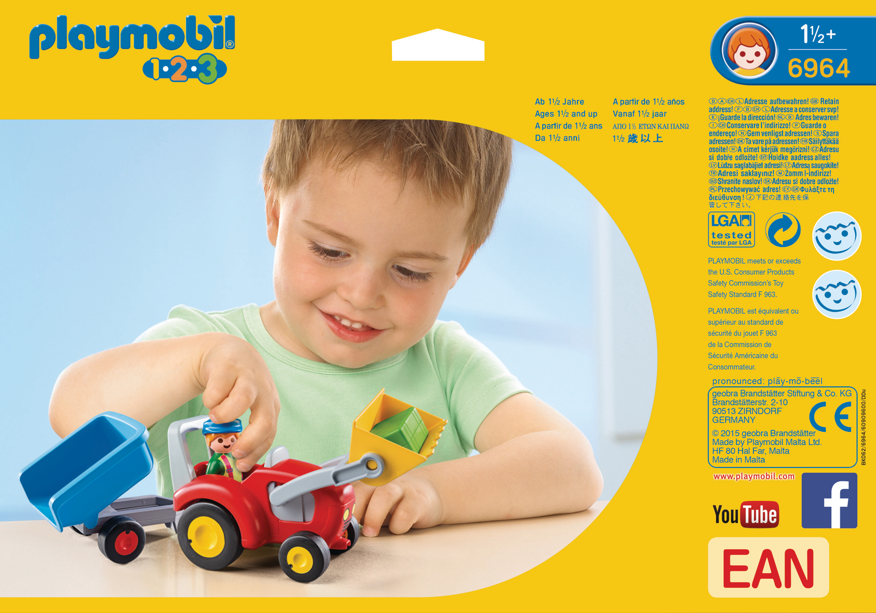 Ein kleiner Junge hält einen Spielzeugtraktor mit Anhänger. Im Hintergrund eine Playmobil-Box.