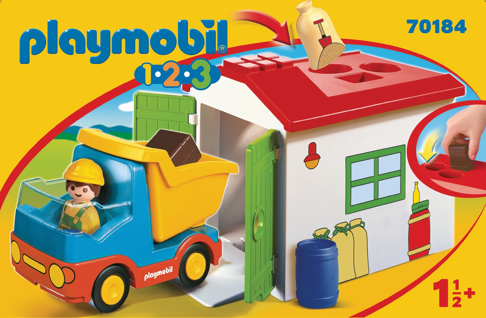 Ein Playmobil-Spielset zeigt einen LKW und ein Haus, mit einer Kinderhand, die interagiert.