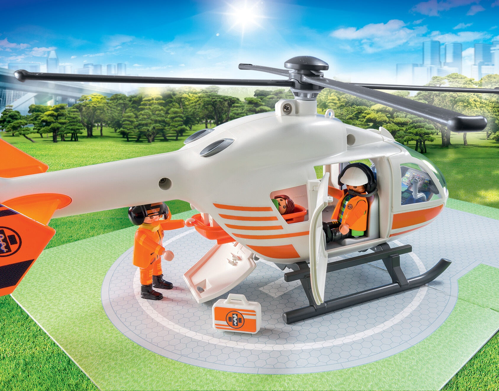Ein Playmobil-Hubschrauber mit zwei Figuren und einem Erste-Hilfe-Kasten auf einem Landeplatz.