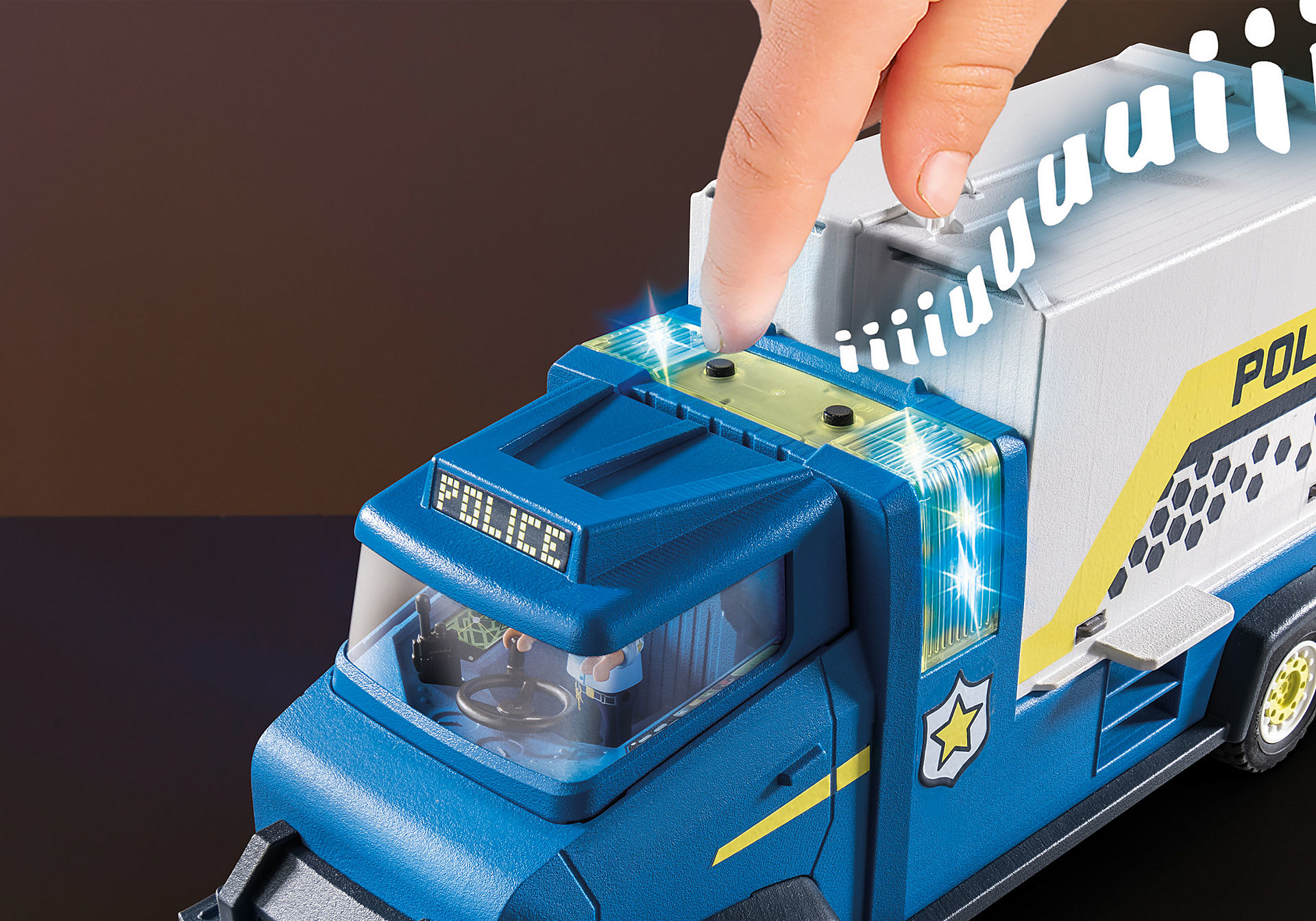 Eine Hand drückt einen Knopf auf einem blau-weißen Spielzeug-Polizeilastwagen mit blinkenden Lichtern.