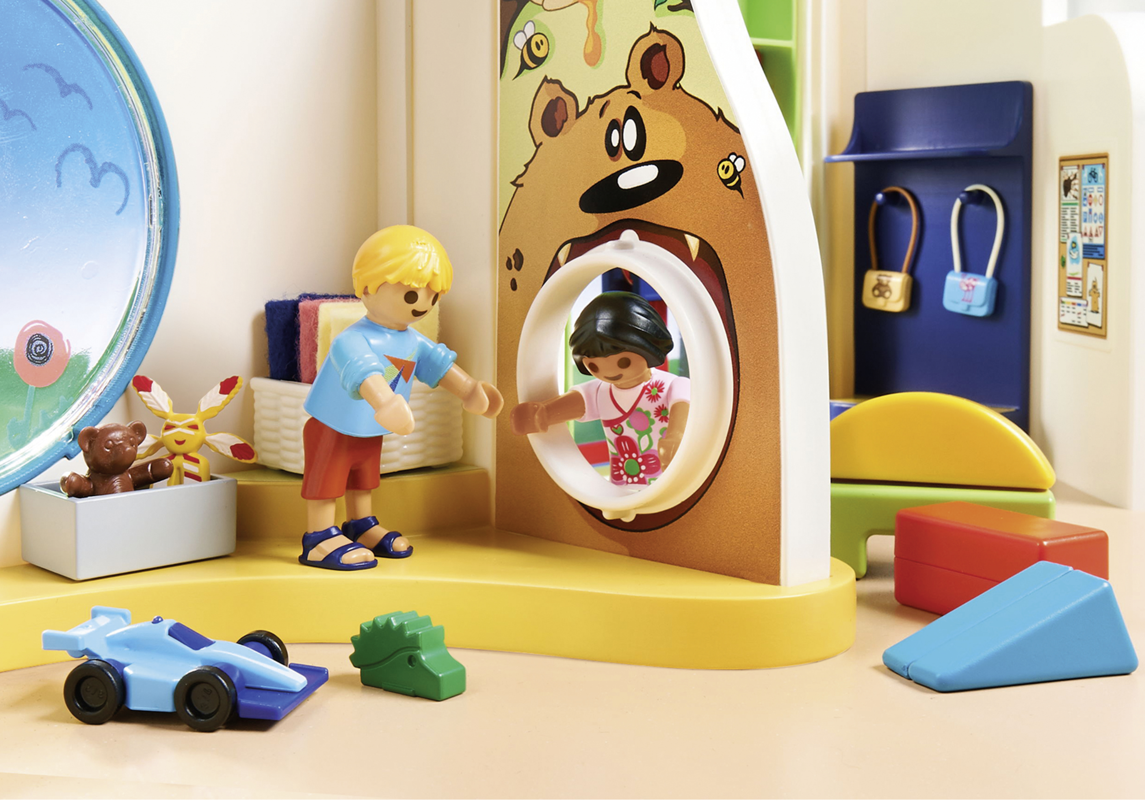 Una scena di casa giochi con due bambini e giocattoli. Visibile una porta a forma di orso.