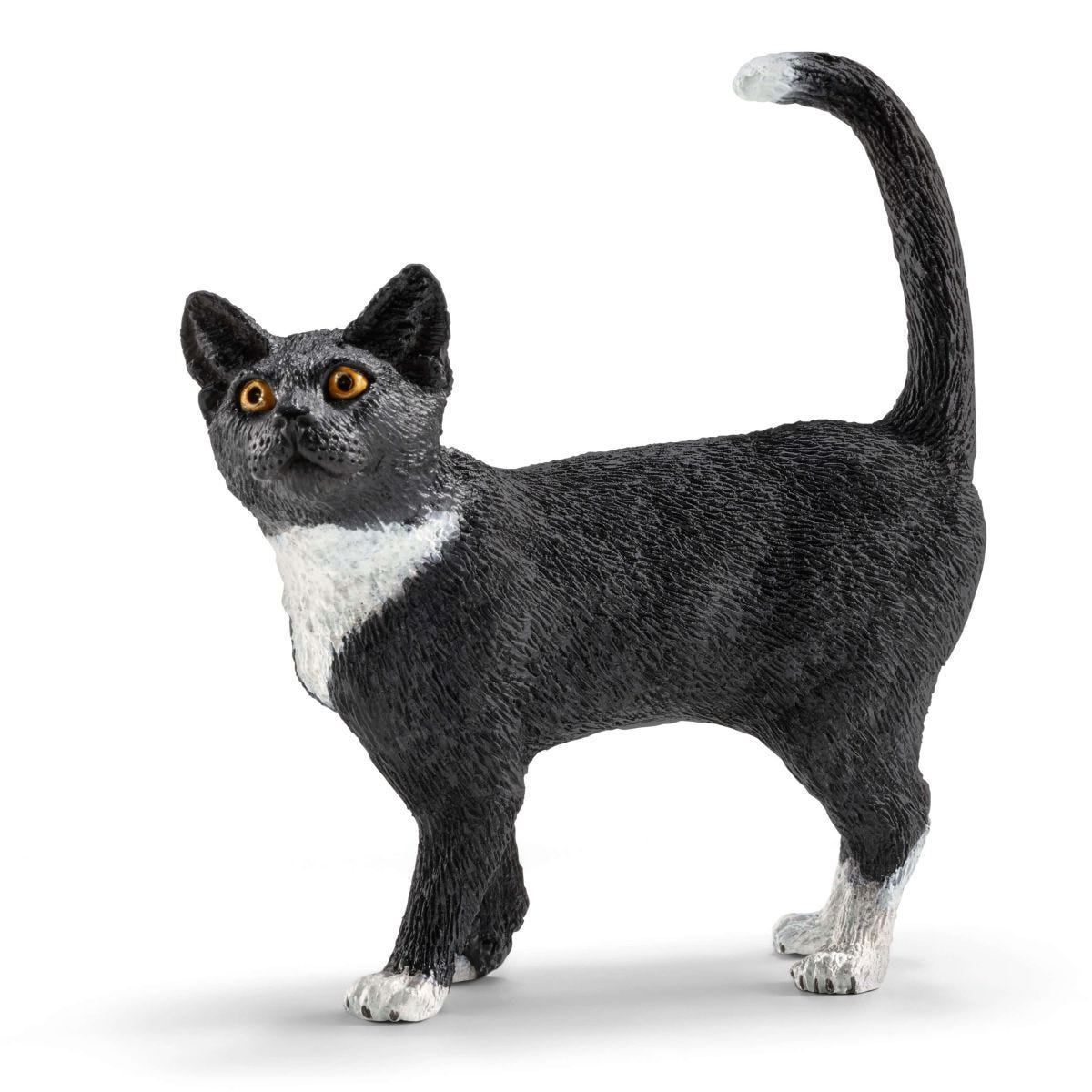 Eine schwarz-weiße Katzenfigur steht und blickt nach oben. Weiße Brust und Pfoten. Gelbe Augen.