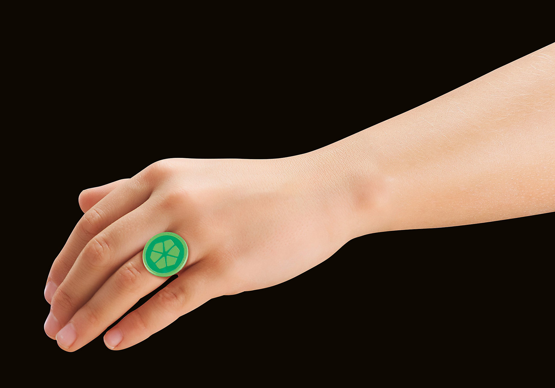 Hand mit grünem Ring mit blütenartigem Design vor schwarzem Hintergrund.