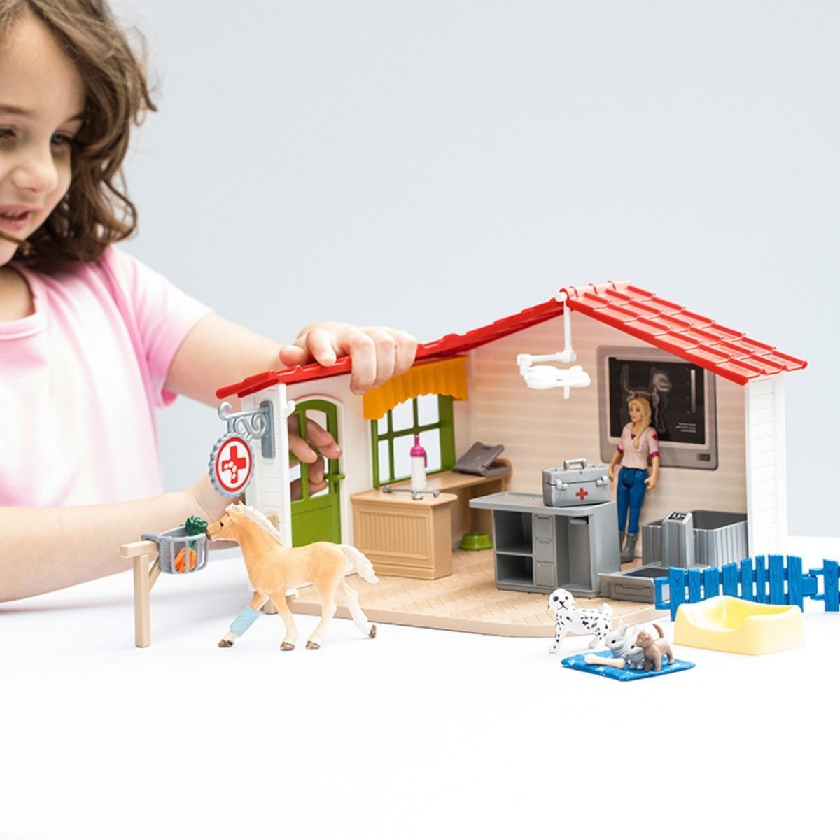 A girl plays with a toy vet clinic. A horse, dog, and woman figurine are in the set.