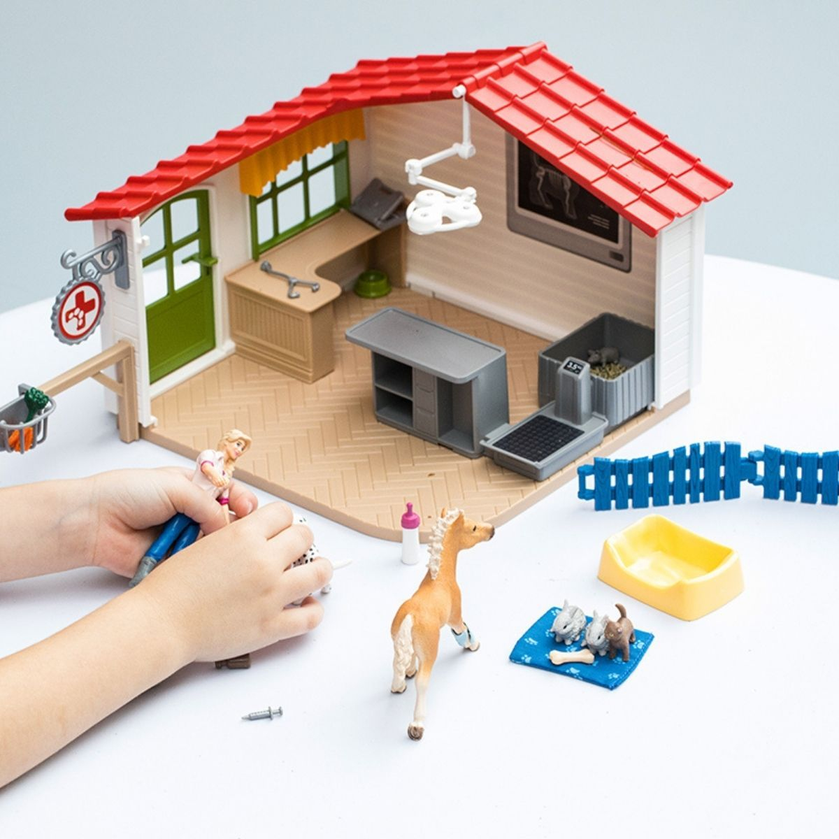 Toy vet clinic with a girl, a dog, a horse, and other toy figures. Red roof.