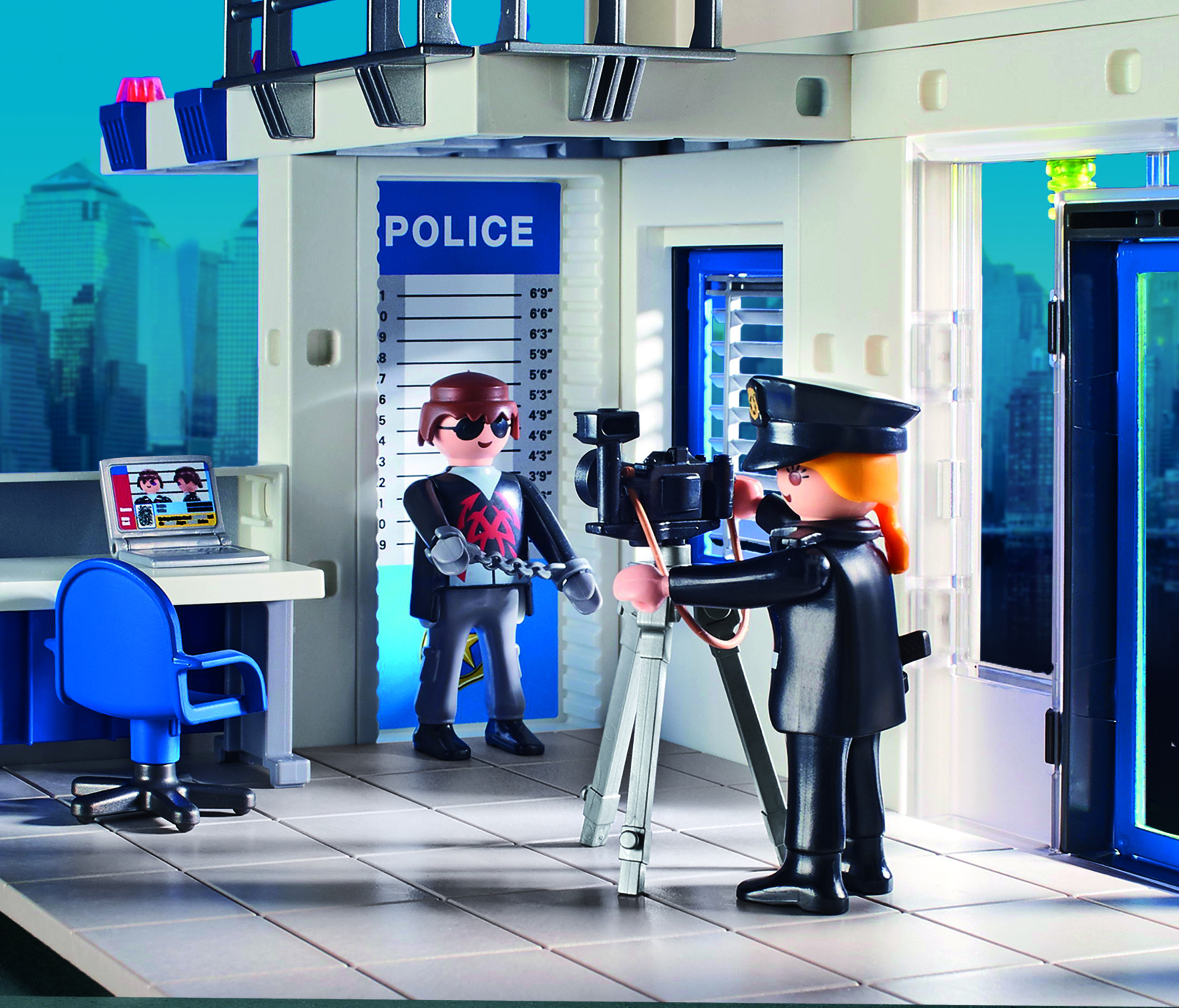 Due agenti di polizia giocattolo in una stazione di polizia che filmano con una telecamera. Un laptop mostra uno schermo.