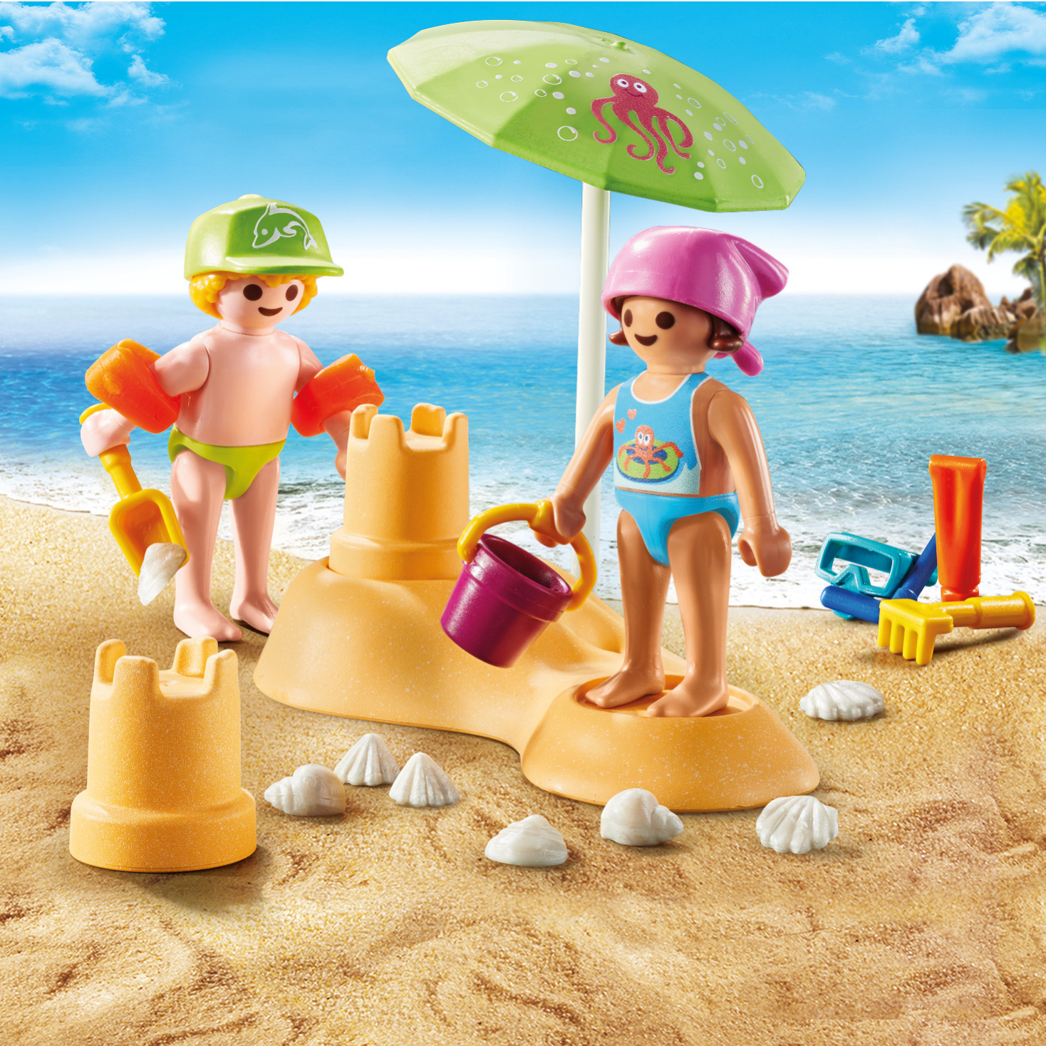 Zwei Playmobil-Figuren am Strand mit Sand, einer Sandburg und einem Sonnenschirm.