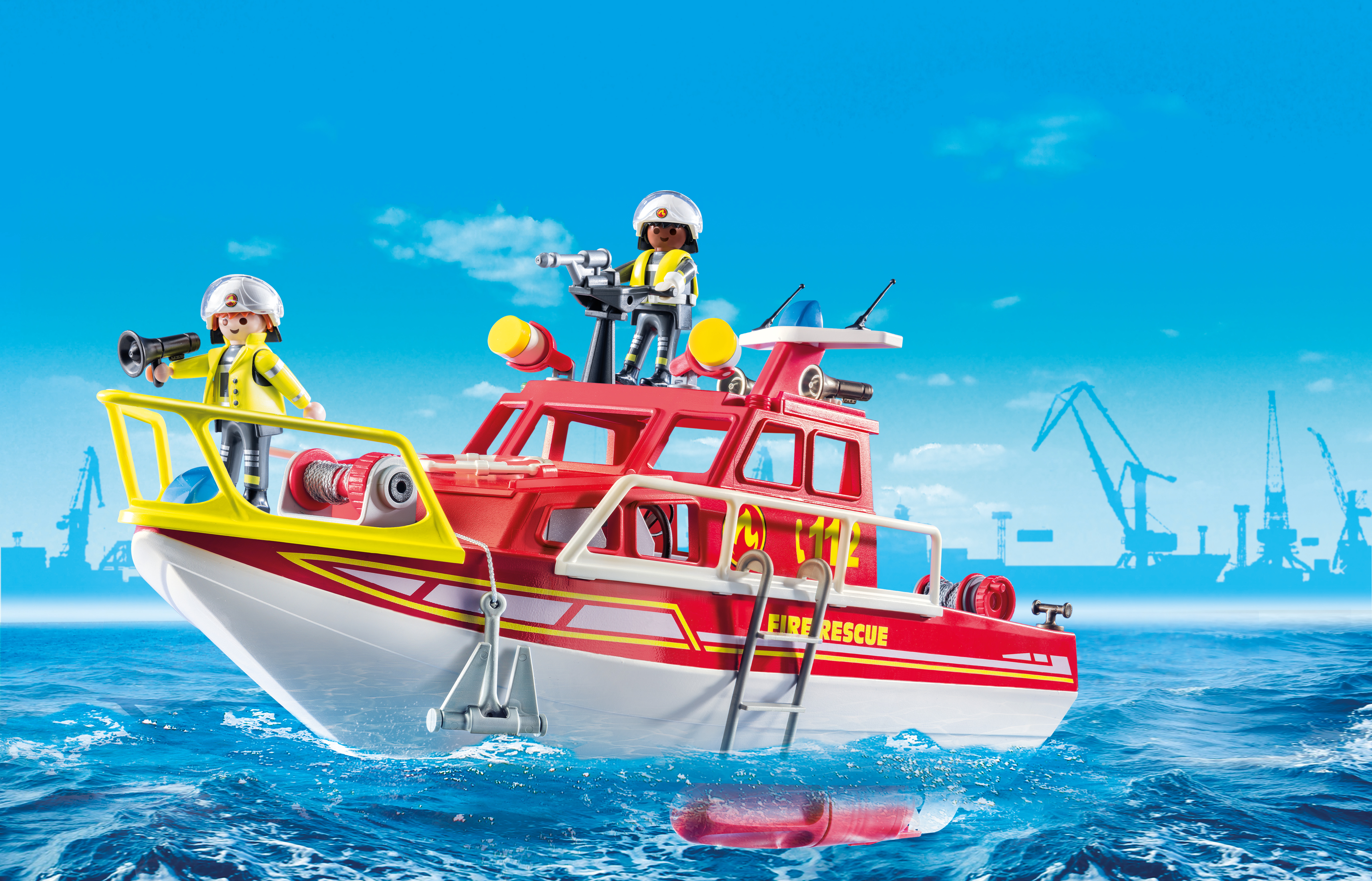 Ein Spielzeug-Feuerwehrboot mit zwei Figuren, Wellen und einem Hafen im Hintergrund.