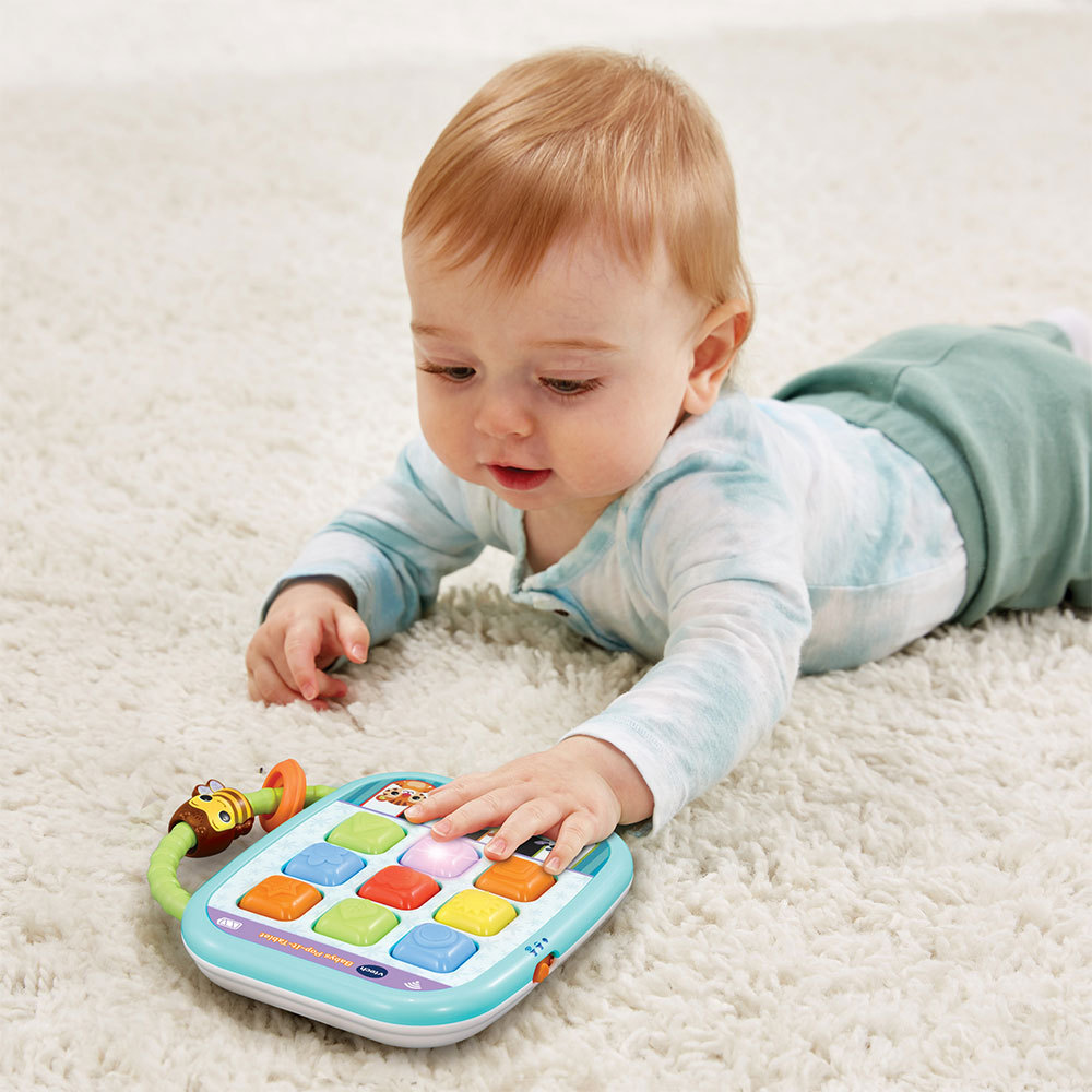Ein Baby liegt auf einem weißen Teppich und spielt mit einem bunten, leuchtenden Tablet-Spielzeug mit einem bienenförmigen Aufsatz.