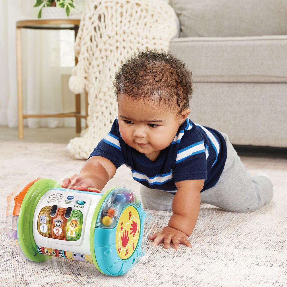 Ein Baby krabbelt auf ein Musikspielzeug mit verschiedenen Knöpfen und Farben zu.