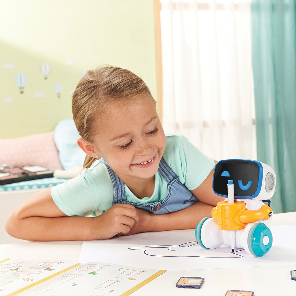 Ein Mädchen betrachtet ein weißes Roboterspielzeug, das auf Papier zeichnet.