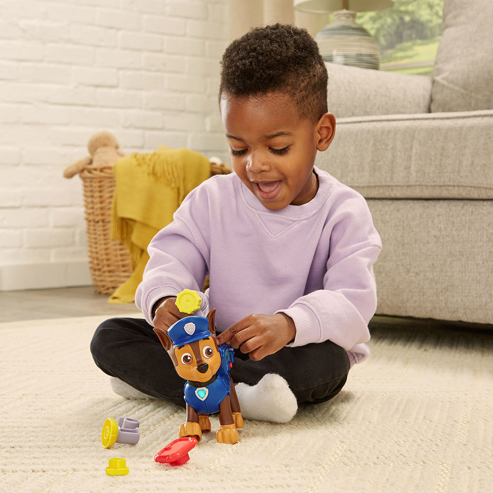 Ein Kind spielt mit einem Paw Patrol-Spielzeug. Das Kind sitzt auf einem Teppich und lächelt.