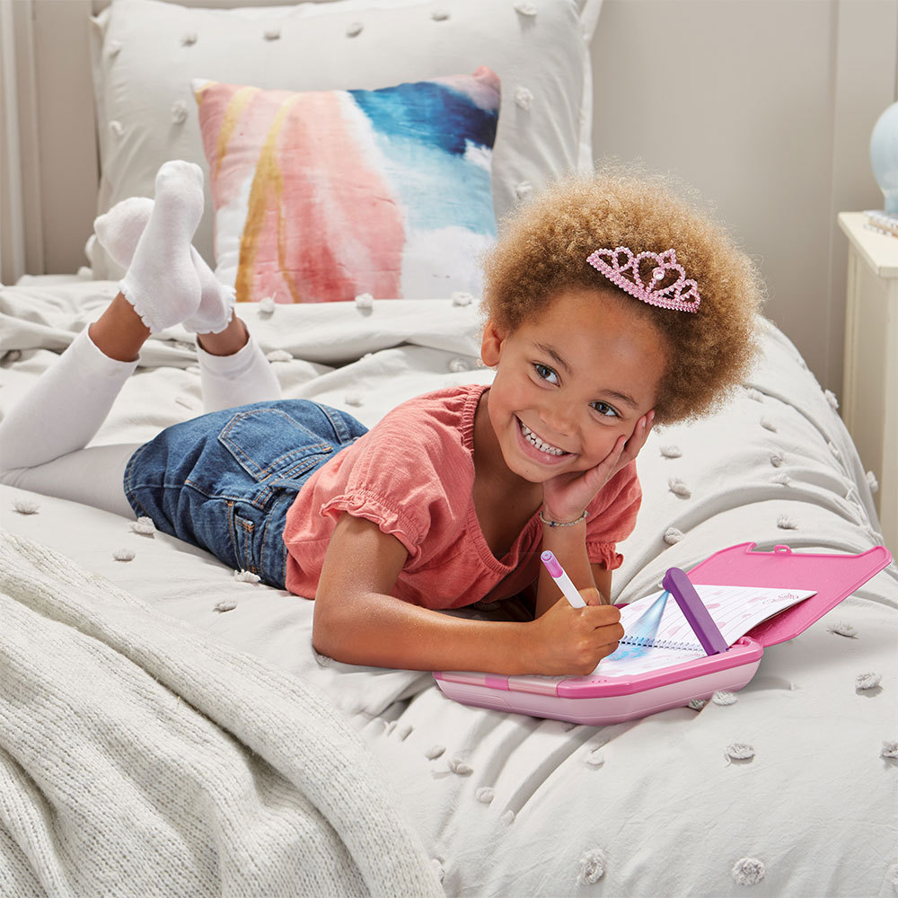 Ein Mädchen in Jeans und rosa Oberteil liegt auf einem Bett und schreibt in ein rosa Notizbuch.