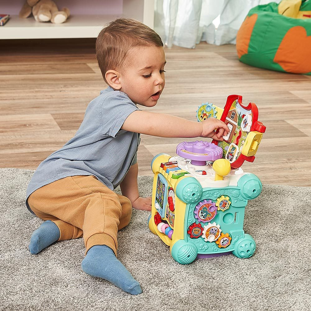 Ein Baby spielt auf einem Teppich mit einem bunten Spielzeugwürfel.