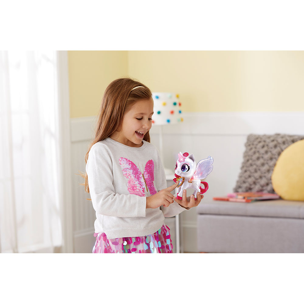 Ein junges Mädchen in einem weiß-rosa Outfit hält und betrachtet ein kleines, beleuchtetes Einhorn-Spielzeug.