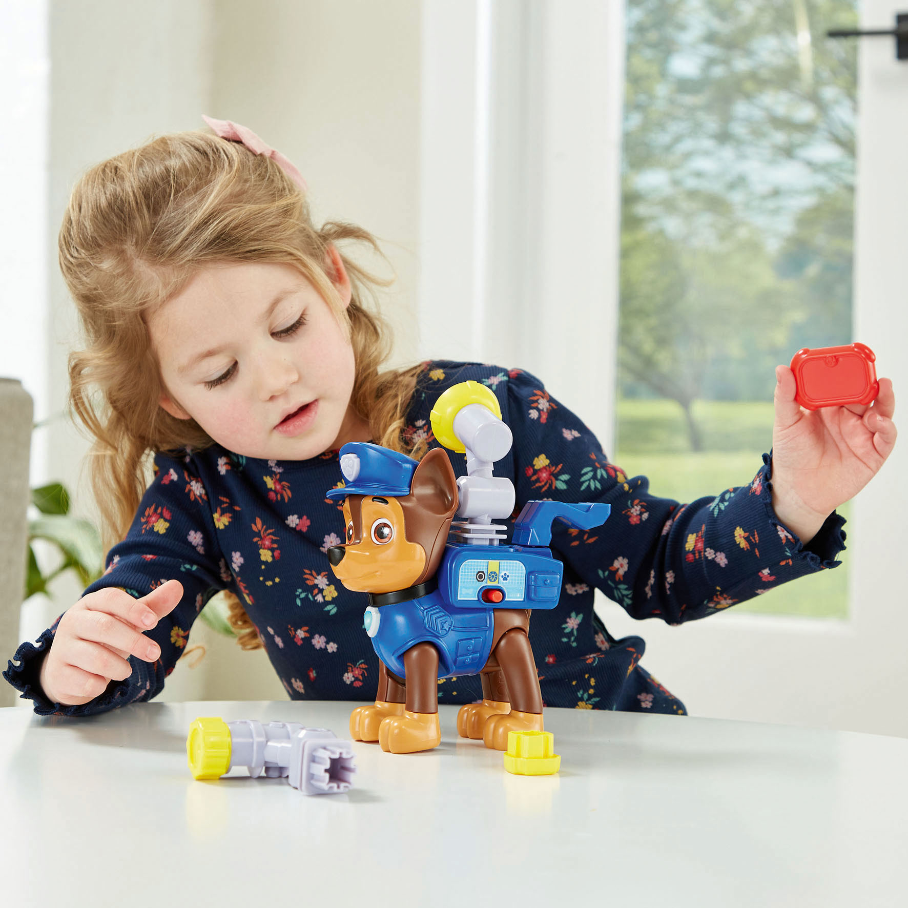 Una bambina che gioca con un giocattolo Chase di Paw Patrol, con attrezzi sul tavolo.