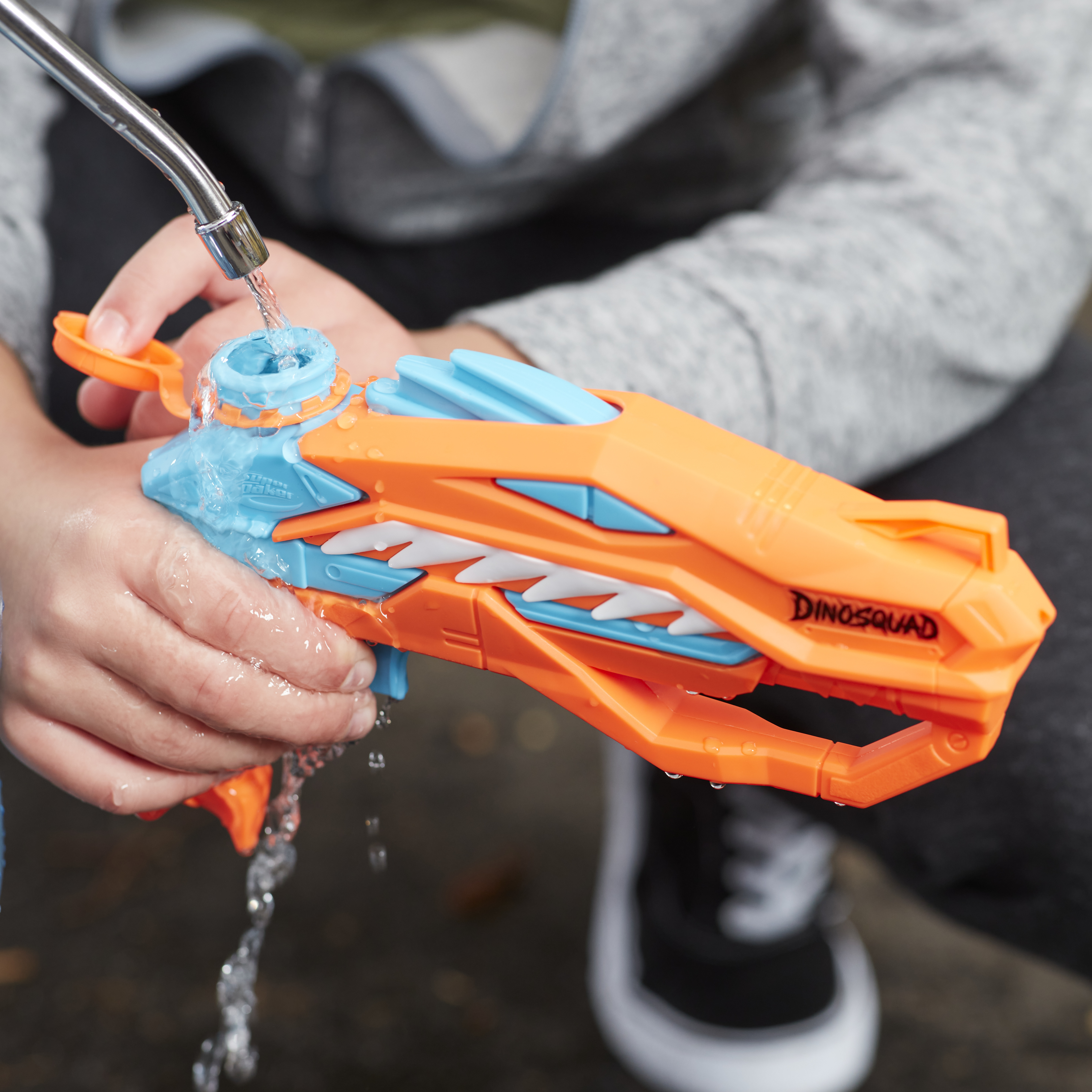 Un bambino gioca con una pistola ad acqua arancione e blu, l'acqua scorre.