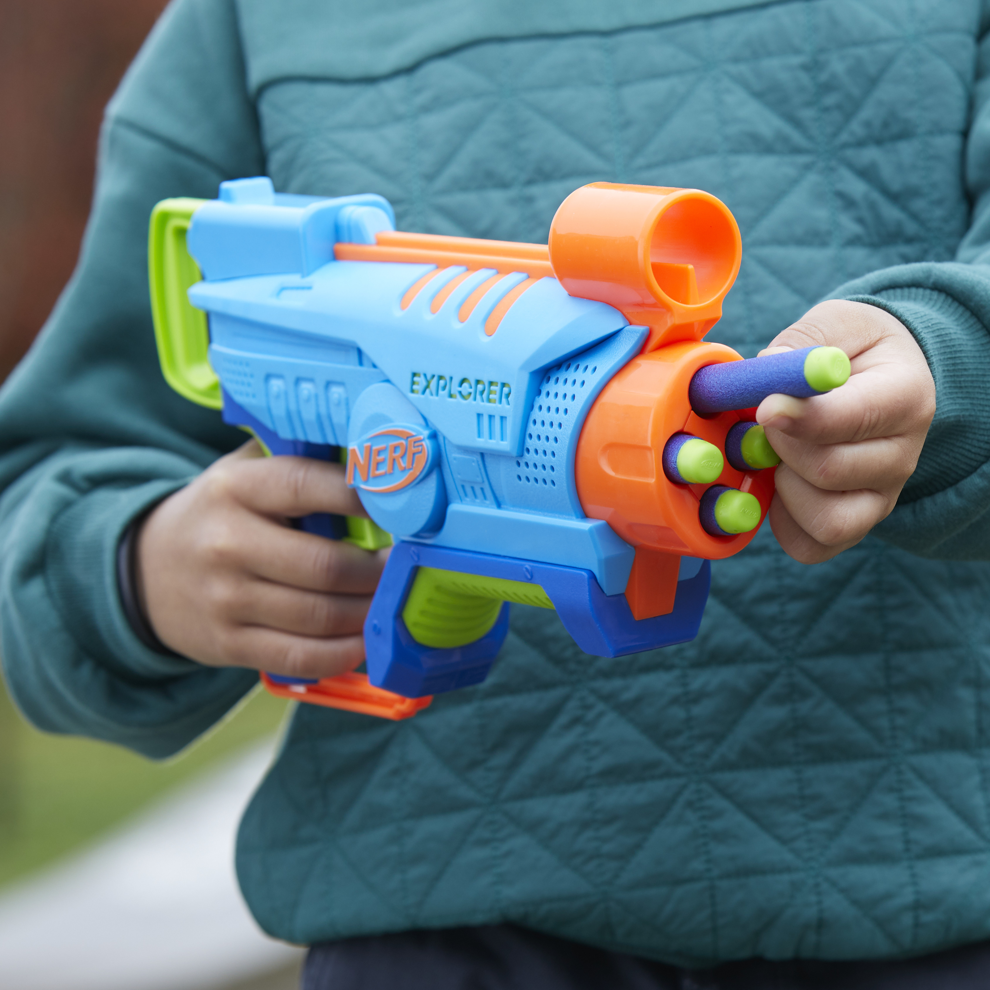 Un juguete de pistola Nerf Explorer azul y naranja sostenido por un niño, con dardos visibles.