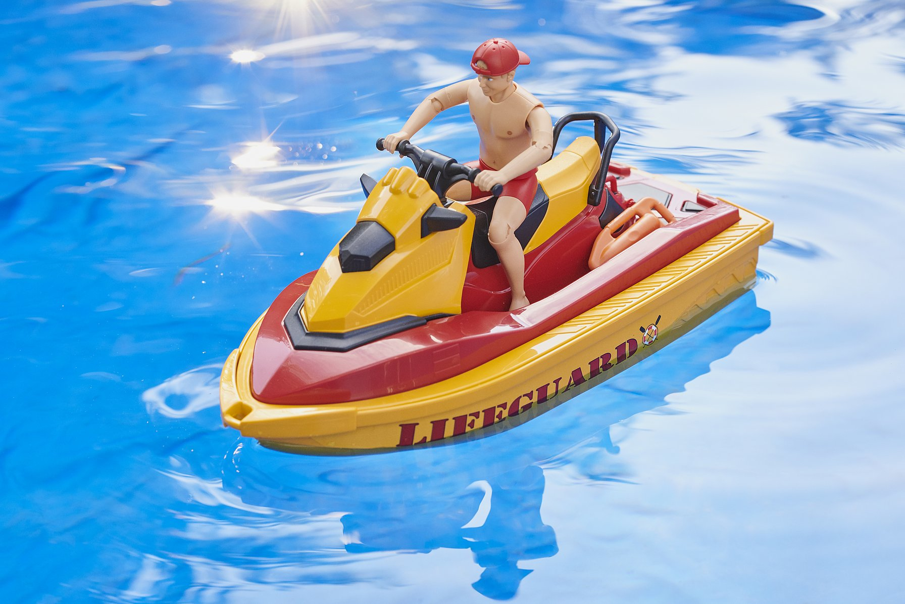 Un bagnino giocattolo su una moto d'acqua gialla e rossa in una piscina. L'acqua è blu e riflette la luce.