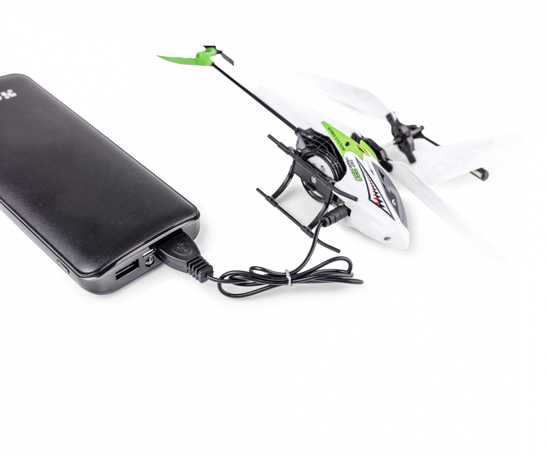 Weiß-grüner Spielzeughelikopter, der mit einer schwarzen Powerbank auf weißem Grund geladen wird.