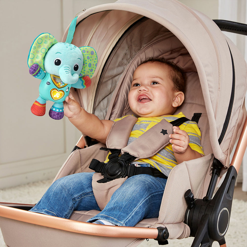 Ein Baby in einem Kinderwagen lächelt und greift nach einem Spielzeug-Elefanten.
