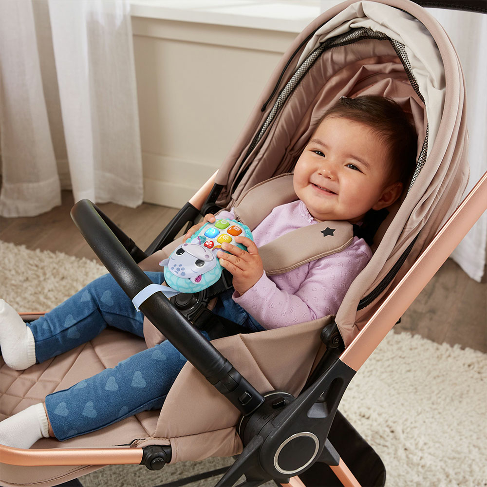 Ein Baby sitzt in einem Kinderwagen und hält ein Spielzeug. Das Baby lächelt. Kinderwagen ist beige und roségold.