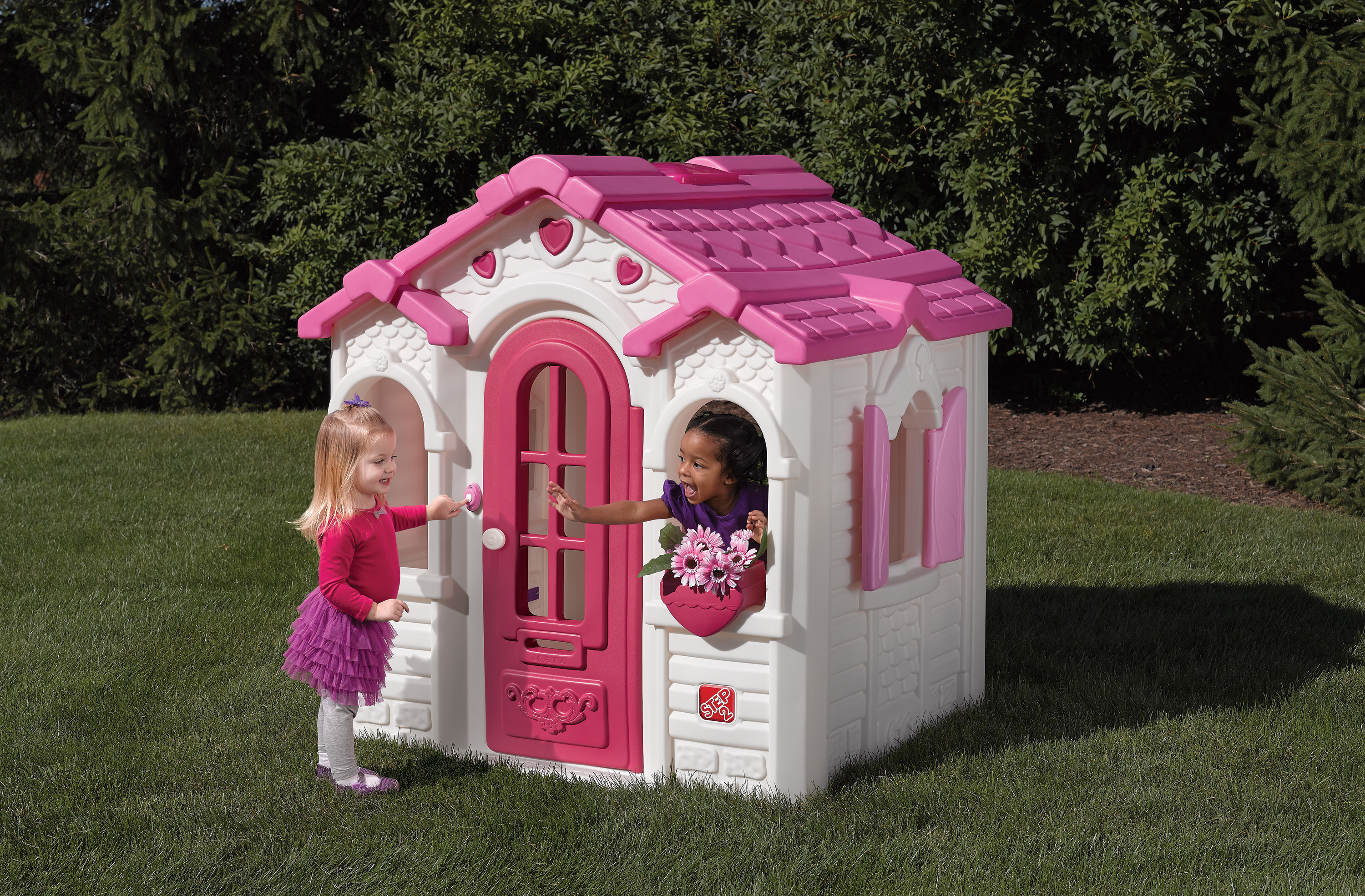 Spielhaus mit zwei Mädchen, rosa Dach, weiße Wände, grünes Gras.